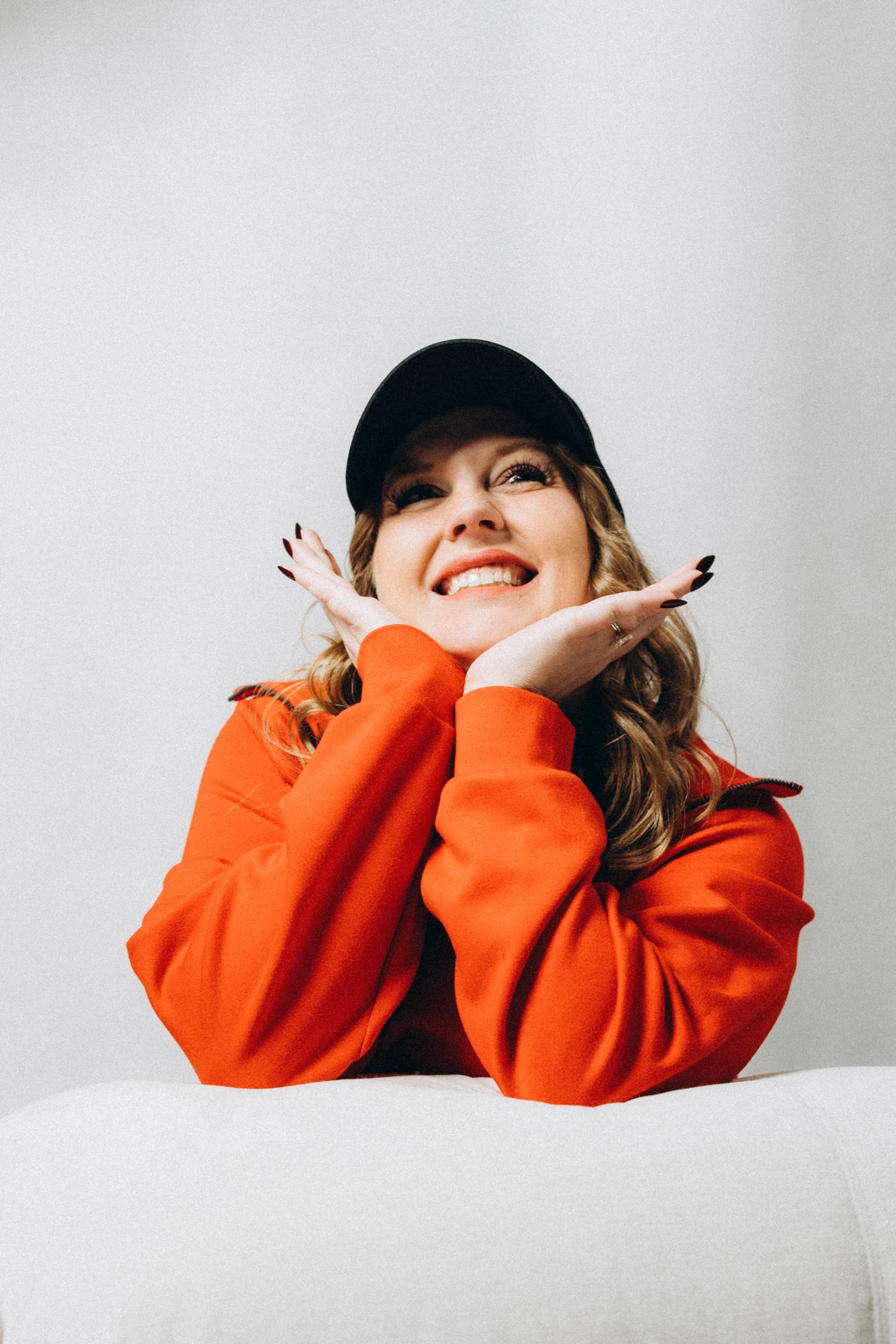 Em Smale smiling in an orange sweatshirt and black cap.
